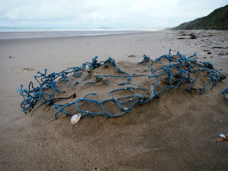 Blue fishing net as flotsam in the sand