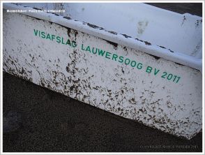 Green writing on grey plastic crate washed up on sandy beach