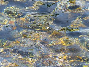 Pebbles under flowing water with small prisms of rainbow colours