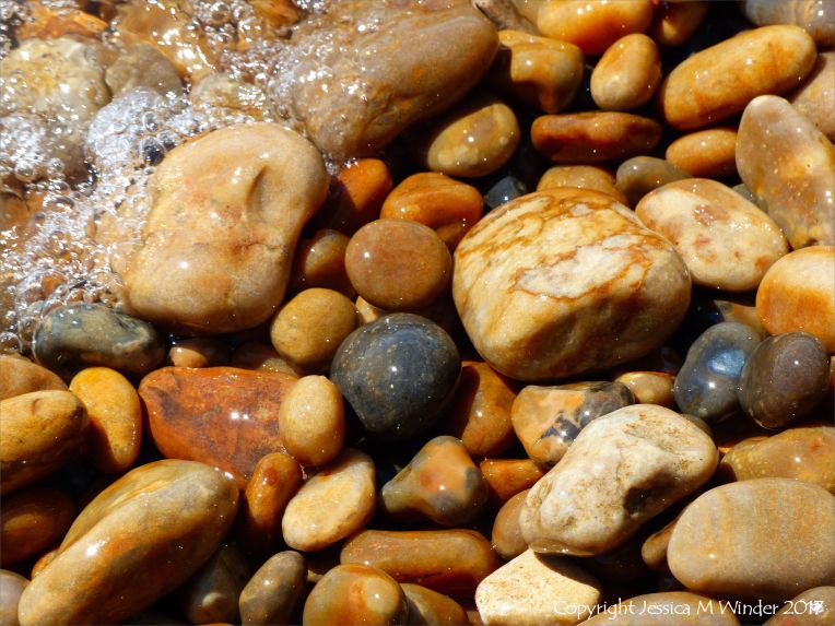 Colourful wet pebbles in the breaking waves at the waters' edge on the beach