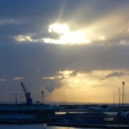 Early light breaking through winter clouds over docks with cranes