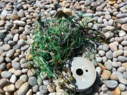 Green fishing rope and reel washed up on a pebble beach