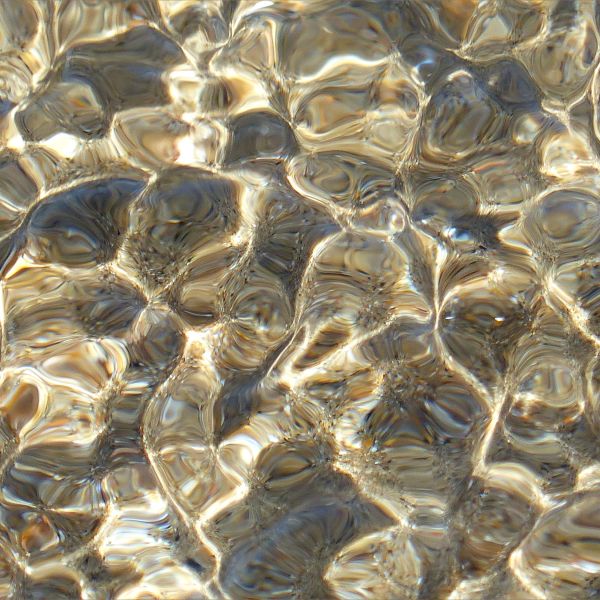 Close-up picture of natural pattern of reflected light on shallow water ripples over sand
